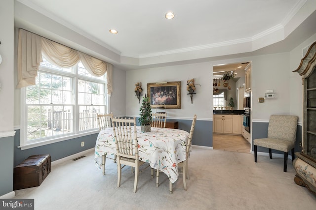 dining room with a raised ceiling, crown molding, and light carpet