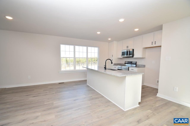 kitchen with sink, an island with sink, light hardwood / wood-style floors, white cabinetry, and stainless steel appliances