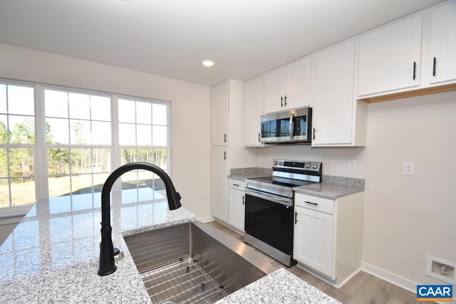 kitchen featuring sink, light stone countertops, appliances with stainless steel finishes, light hardwood / wood-style floors, and white cabinetry