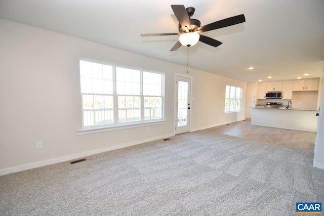 unfurnished living room with ceiling fan, sink, and light colored carpet