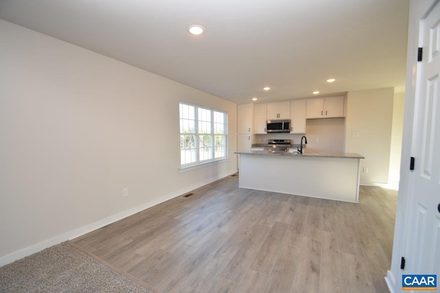 kitchen with light stone countertops, appliances with stainless steel finishes, sink, light hardwood / wood-style floors, and white cabinetry