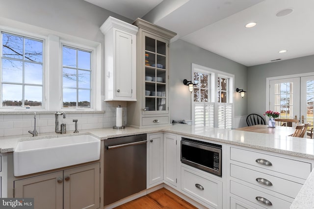 kitchen featuring kitchen peninsula, light stone counters, stainless steel appliances, sink, and light hardwood / wood-style floors