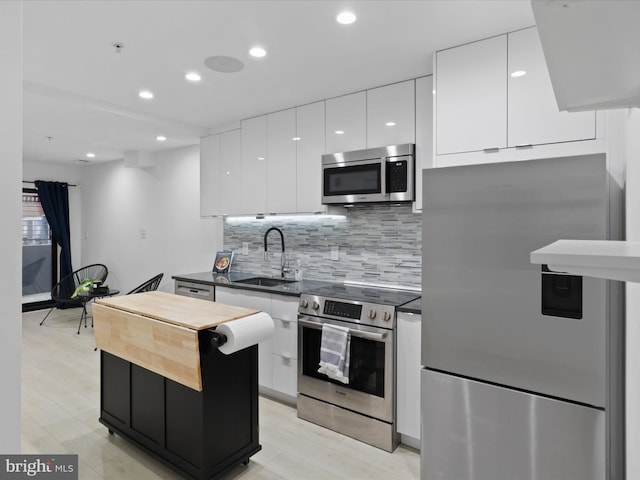 kitchen with white cabinets, sink, light wood-type flooring, appliances with stainless steel finishes, and tasteful backsplash