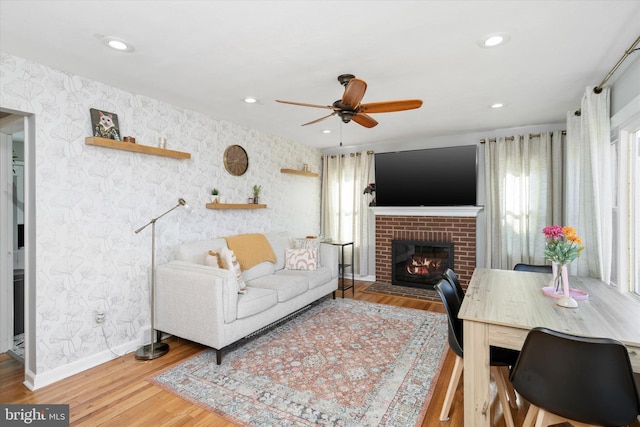 living room featuring hardwood / wood-style flooring, ceiling fan, and a brick fireplace