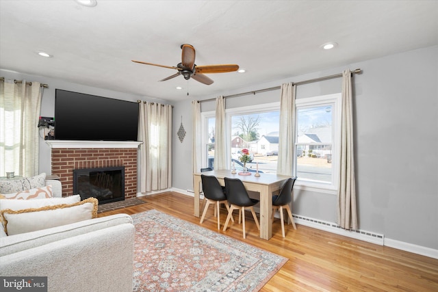 living room featuring a fireplace, light hardwood / wood-style flooring, baseboard heating, and ceiling fan