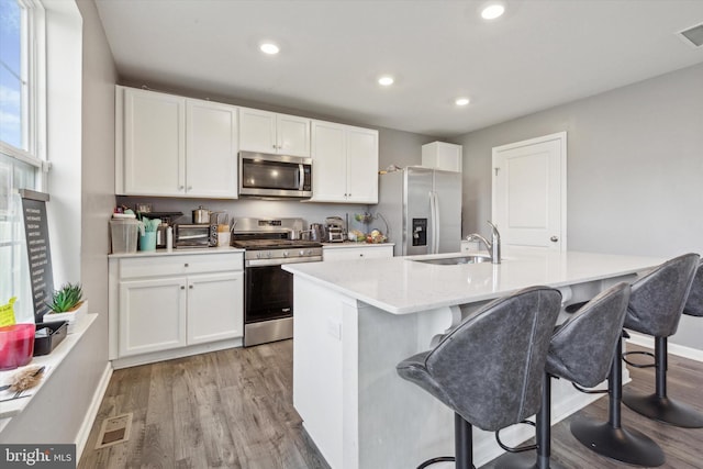 kitchen with a kitchen breakfast bar, sink, light hardwood / wood-style flooring, an island with sink, and appliances with stainless steel finishes