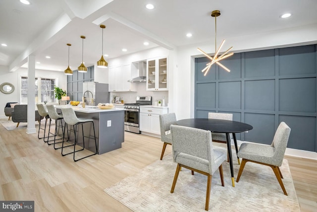 kitchen featuring appliances with stainless steel finishes, wall chimney range hood, a center island with sink, white cabinets, and hanging light fixtures