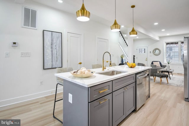 kitchen with appliances with stainless steel finishes, gray cabinetry, a kitchen island with sink, sink, and pendant lighting