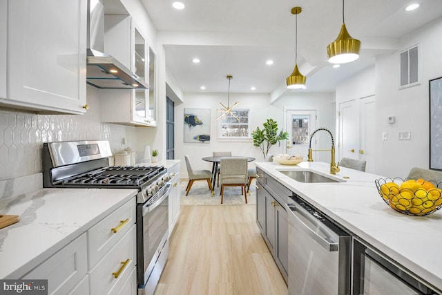 kitchen featuring sink, wall chimney exhaust hood, hanging light fixtures, stainless steel appliances, and white cabinets