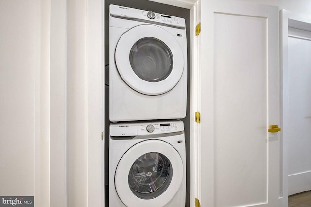 clothes washing area with hardwood / wood-style floors and stacked washer and dryer