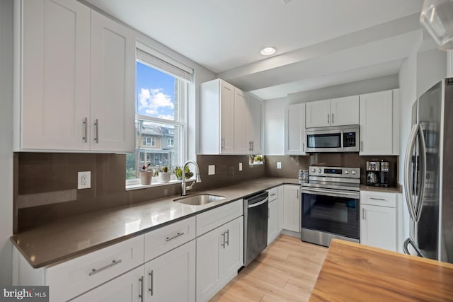 kitchen featuring white cabinets, sink, light wood-type flooring, appliances with stainless steel finishes, and tasteful backsplash