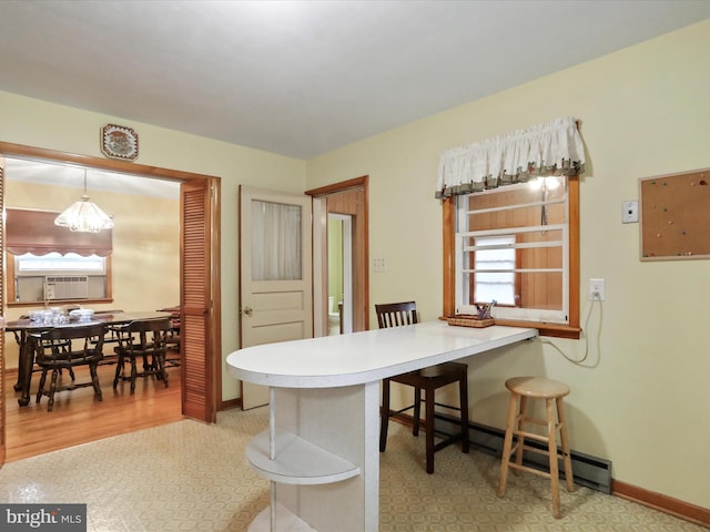 interior space featuring a baseboard heating unit, hanging light fixtures, light wood-type flooring, kitchen peninsula, and a breakfast bar area