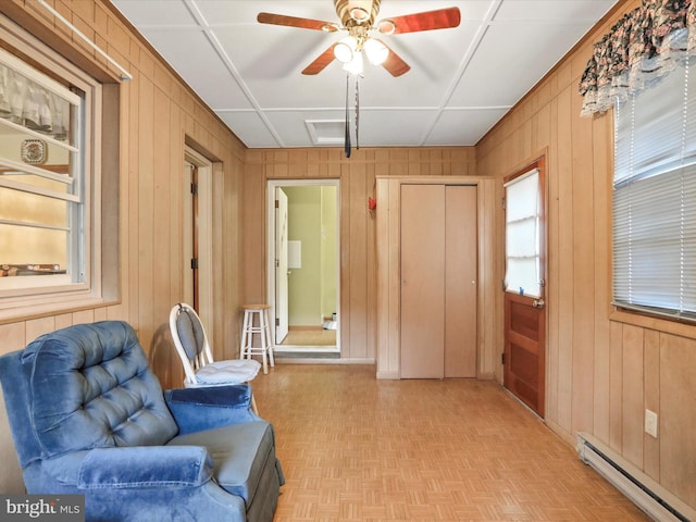 living area featuring light parquet flooring, ceiling fan, a baseboard heating unit, and wood walls