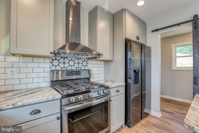 kitchen with backsplash, wall chimney range hood, light hardwood / wood-style flooring, gray cabinets, and stainless steel appliances