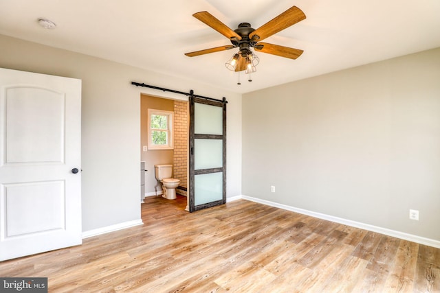 unfurnished bedroom featuring a barn door, ensuite bathroom, ceiling fan, and light hardwood / wood-style floors