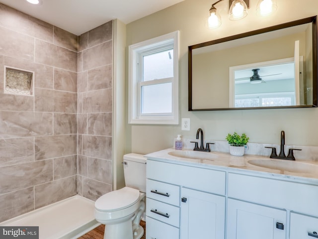 bathroom with vanity, toilet, a tile shower, and ceiling fan