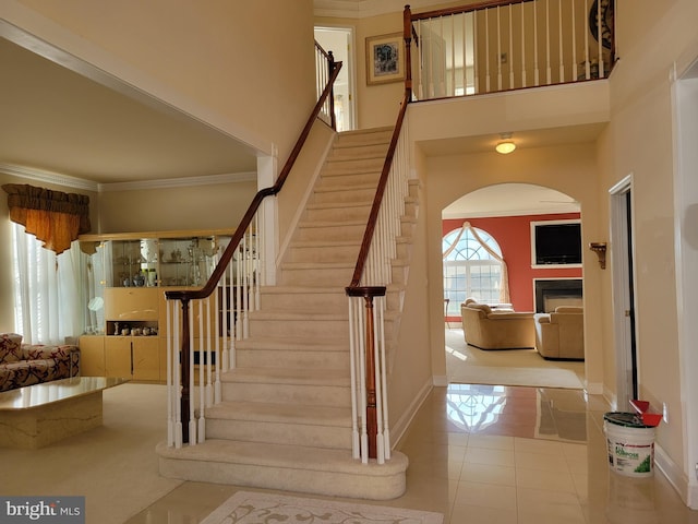 staircase featuring tile patterned floors, ornamental molding, and a towering ceiling