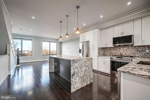 kitchen featuring light stone countertops, appliances with stainless steel finishes, ornamental molding, white cabinets, and a kitchen island