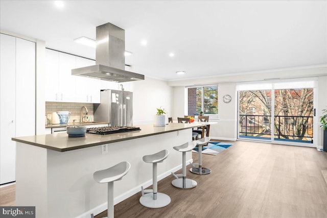 kitchen with a kitchen bar, light wood-type flooring, island range hood, stainless steel appliances, and white cabinets