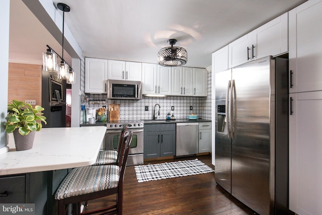 kitchen with kitchen peninsula, appliances with stainless steel finishes, tasteful backsplash, decorative light fixtures, and white cabinets