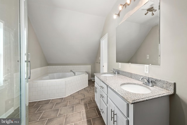 bathroom with tile patterned floors, tiled tub, vanity, and lofted ceiling