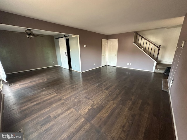 unfurnished living room featuring a barn door, ceiling fan, and dark wood-type flooring