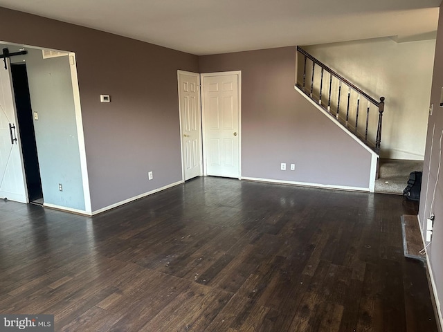 unfurnished living room featuring a barn door and dark hardwood / wood-style flooring