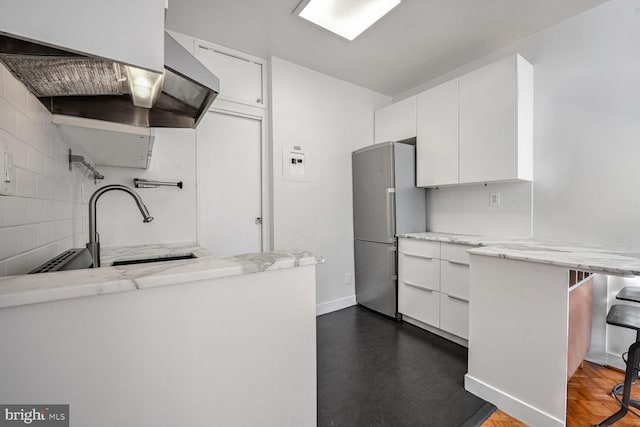 kitchen with a breakfast bar area, stainless steel refrigerator, light stone countertops, and white cabinets