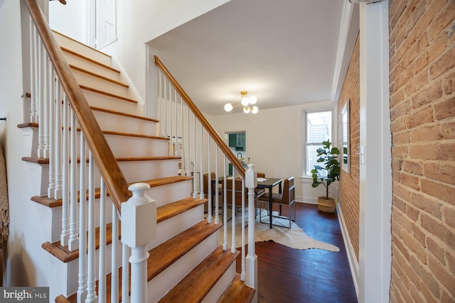 stairs featuring hardwood / wood-style flooring, a notable chandelier, and brick wall