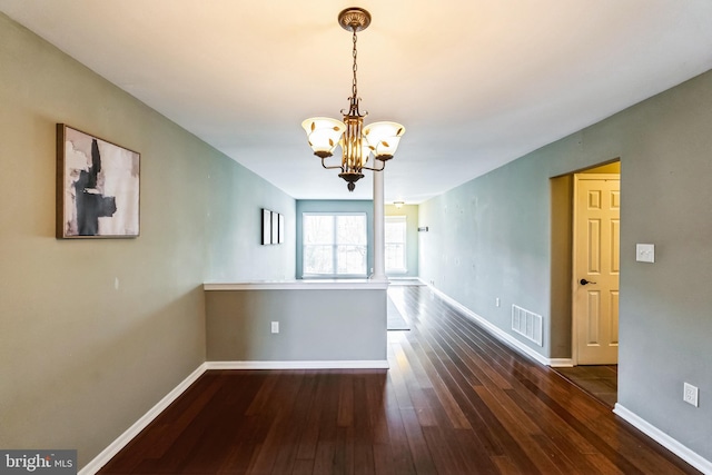 spare room featuring dark wood-type flooring and a chandelier