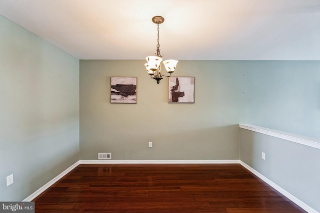 empty room with a notable chandelier and dark wood-type flooring