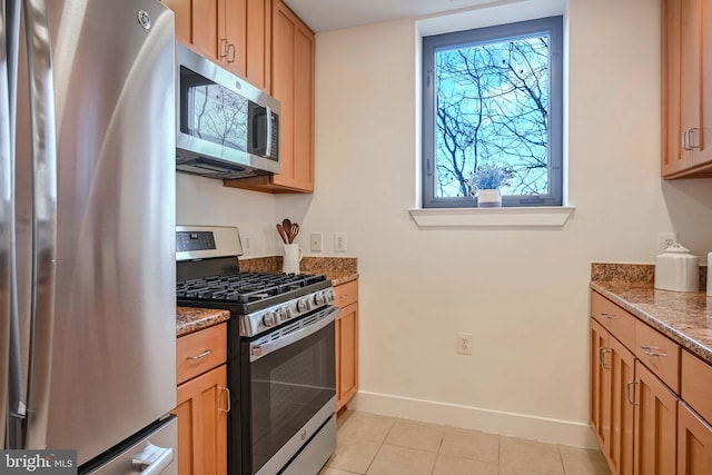 kitchen with appliances with stainless steel finishes, light tile patterned floors, and dark stone countertops