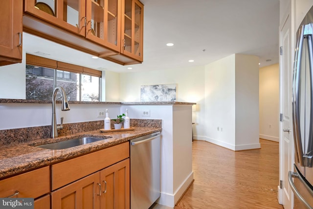 kitchen featuring dark stone counters, sink, stainless steel appliances, and light hardwood / wood-style flooring