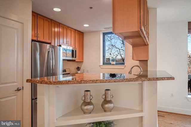 kitchen featuring light stone countertops, kitchen peninsula, light wood-type flooring, and appliances with stainless steel finishes