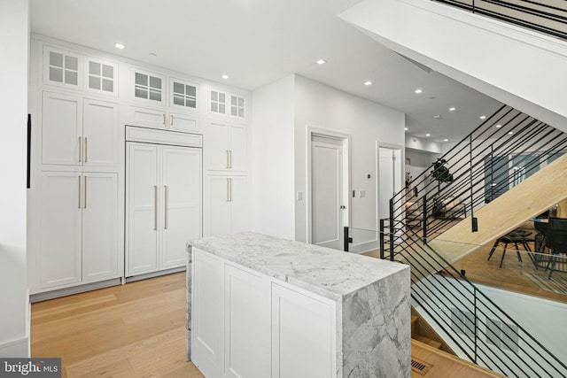 kitchen with white cabinetry, a center island, light stone countertops, and light hardwood / wood-style floors