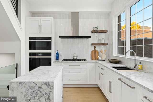 kitchen with white cabinets, wall chimney range hood, sink, light wood-type flooring, and light stone counters