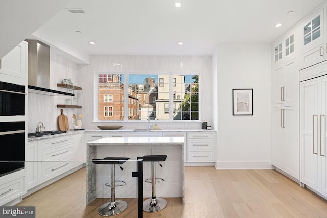 kitchen with white cabinets, light hardwood / wood-style floors, light stone countertops, and a breakfast bar area