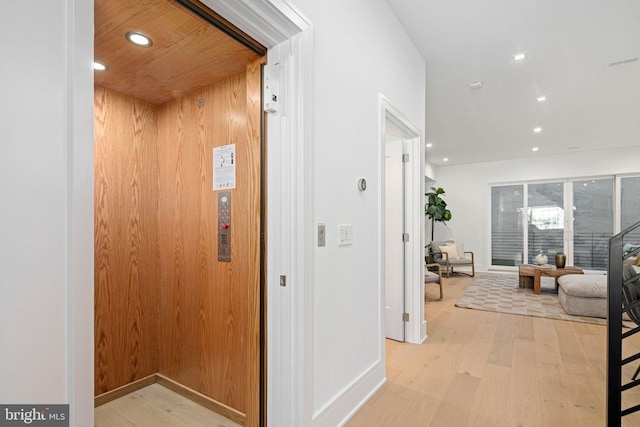 hallway featuring elevator, light hardwood / wood-style flooring, and wooden walls