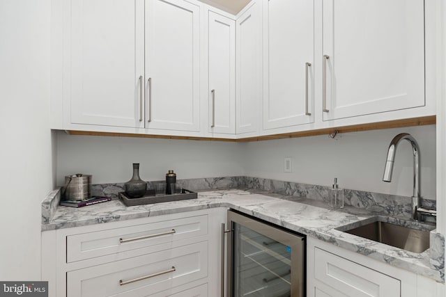 kitchen featuring white cabinets, light stone counters, beverage cooler, and sink