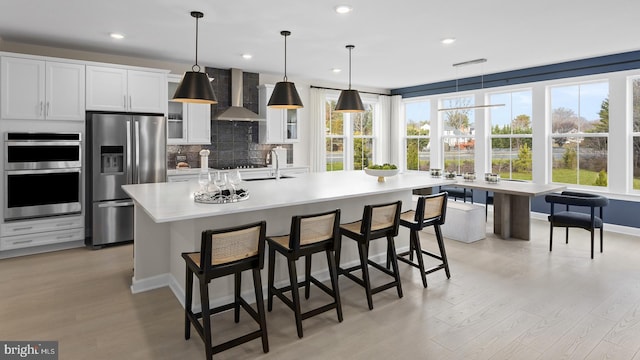 kitchen featuring a kitchen bar, appliances with stainless steel finishes, light wood-type flooring, wall chimney range hood, and an island with sink