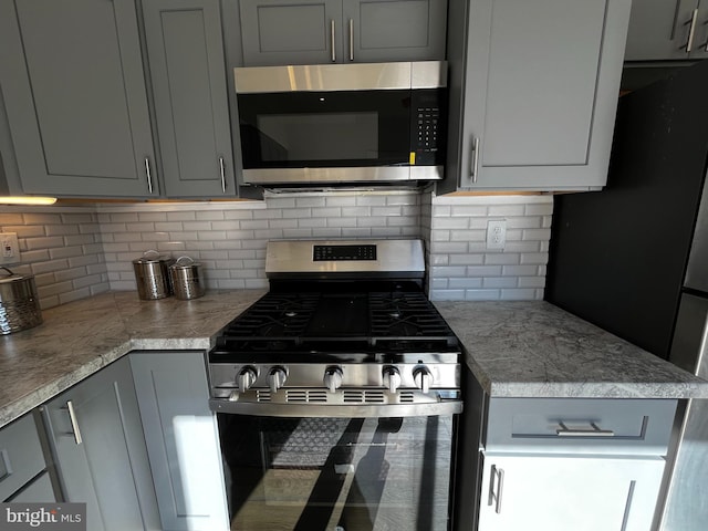 kitchen with gray cabinets, light stone counters, stainless steel appliances, and tasteful backsplash