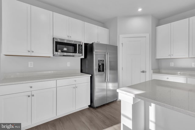 kitchen with white cabinets, appliances with stainless steel finishes, light wood-type flooring, and light stone countertops