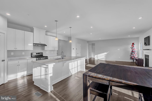 kitchen featuring gas stove, dark hardwood / wood-style flooring, decorative light fixtures, a kitchen island with sink, and white cabinets