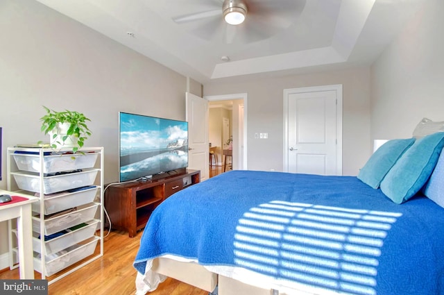 bedroom featuring ceiling fan, wood-type flooring, and a tray ceiling