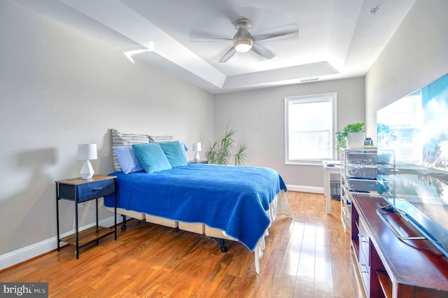 bedroom with a raised ceiling, ceiling fan, and light hardwood / wood-style floors