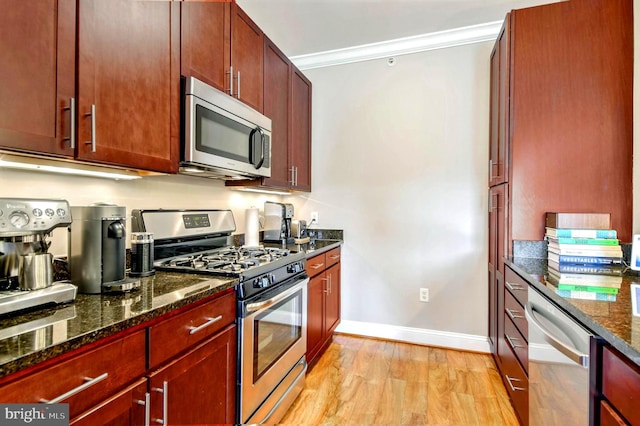 kitchen featuring ornamental molding, dark stone counters, light wood-type flooring, and appliances with stainless steel finishes