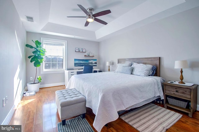 bedroom with a raised ceiling, ceiling fan, and hardwood / wood-style floors