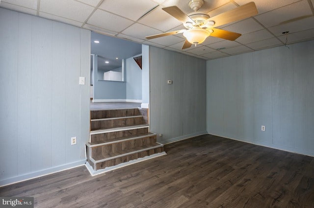 basement with a paneled ceiling, ceiling fan, and dark wood-type flooring