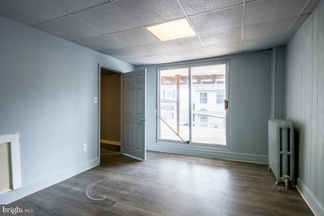 spare room with a paneled ceiling, dark hardwood / wood-style floors, wooden walls, and radiator