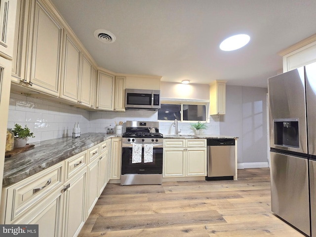 kitchen with sink, stainless steel appliances, cream cabinets, light hardwood / wood-style floors, and decorative backsplash